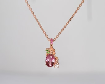 May include: A rose gold necklace with a pendant featuring a large oval pink gemstone, accented by smaller pink, green, and white gemstones. The chain is delicate and the pendant is intricately designed.