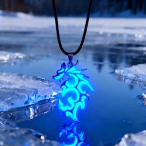 May include: A glowing blue dragon pendant necklace. The pendant is intricately designed with swirling patterns and a dragon silhouette. The necklace has a black cord and a silver-colored clasp. The pendant is illuminated with a bright blue light.