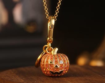 May include: A gold-colored necklace featuring a pumpkin pendant. The pumpkin is orange with embedded orange crystals, a carved face, and a small stem. The pendant hangs from a gold chain, perfect for Halloween.