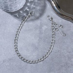 May include: A silver-colored chain with a cross charm. The chain has a lobster clasp on each end. The cross charm is a simple, open design. The chain is likely used as a decorative accessory.