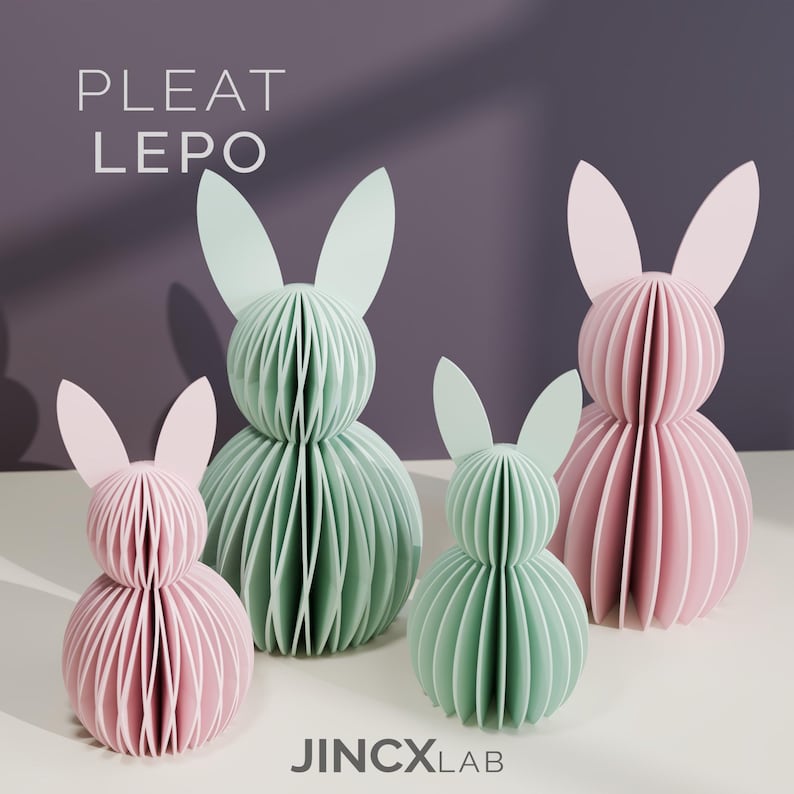 Puede incluir: Cuatro esculturas de conejos de papel en colores pastel. Dos son rosas y dos son verde menta. Los conejos tienen un dise&ntilde;o plisado y est&aacute;n sobre una superficie blanca contra un fondo p&uacute;rpura. El texto "PLEAT LEPO" y "JINCXLAB" es visible.