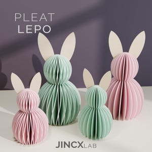 Puede incluir: Cuatro esculturas de conejos de papel en colores pastel. Dos son rosas y dos verde menta, con orejas color crema. Los conejos est&aacute;n hechos de papel plisado, con el texto "PLEAT LEPO" y "JINCXLAB" visibles.