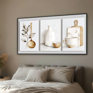 May include: A triptych wall art piece in a black frame featuring three white panels. The left panel shows a gold spoon and a leafy branch. The centre panel displays a white bottle and a small bowl. The right panel depicts a cup and a cutting board.