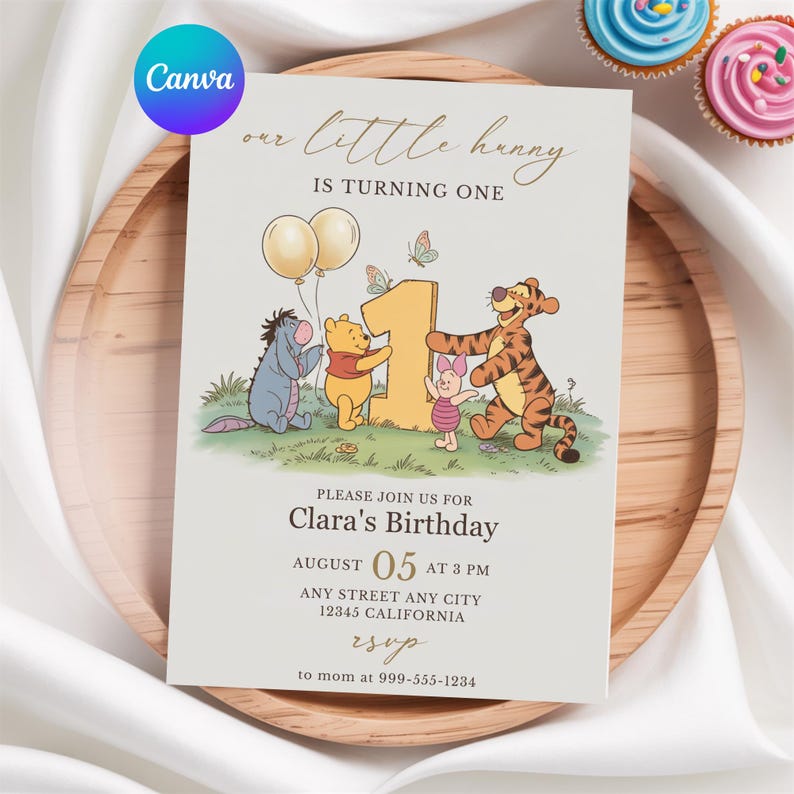 Op de afbeelding: Een lichtbeige verjaardagsuitnodiging met Winnie de Poeh-personages. De tekst luidt "our little hunny is turning one" en bevat feestdetails. Twee cupcakes met blauwe en roze glazuur staan op de achtergrond.