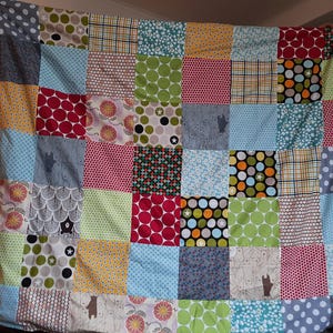 Puede incluir: Un edredón patchwork con cuadrados coloridos. Los diseños incluyen lunares, flores y osos. El edredón se muestra, destacando su calidad artesanal y la mezcla de telas, con unas dimensiones aproximadas de 150 cm x 180 cm.