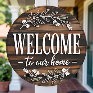 Puede incluir: Cartel de bienvenida redondo de madera con las palabras "WELCOME - to our home -" en blanco. El cartel tiene un fondo marrón oscuro con un patrón de vetas de madera y detalles florales blancos.