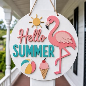 Op de afbeelding: Ronde, witte houten bord met de woorden "Hello SUMMER" in roze en turquoise letters. Het heeft een roze flamingo, een gele zon, een strandbal en een ijsje. Opgehangen aan een jute touw.