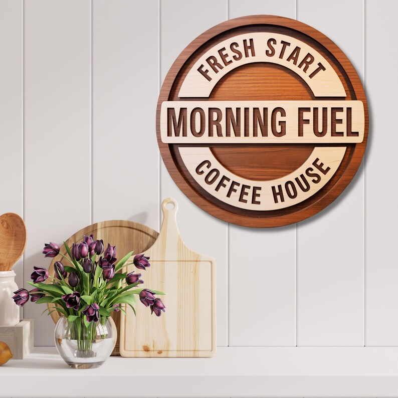 Puede incluir: Un letrero redondo de madera con las palabras "FRESH START", "MORNING FUEL" y "COFFEE HOUSE". El letrero es marr&oacute;n y marr&oacute;n claro, con vetas de madera natural. Cuelga de una pared blanca.