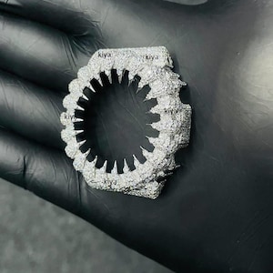 May include: A silver-toned, diamond-encrusted ring with a unique, jagged design. The ring features a central opening with pointed edges, surrounded by a textured, gem-studded band. The word "kiya" is visible on the ring.