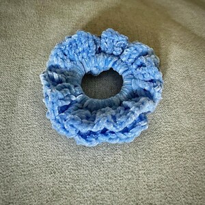 May include: A light blue scrunchie made of a soft, plush material. The hair accessory is circular with a hole in the center. The scrunchie is a solid color and appears to be made of a velvet-like fabric.