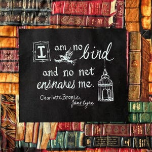 May include: A black square with white text and illustrations, including a bird and a cage, is centered on a patchwork of fabric books. The text reads "I am no bird and no net ensnares me." The quote is from Charlotte Bronte's "Jane Eyre."