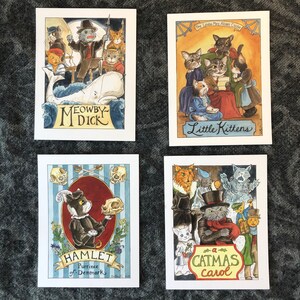 May include: Four illustrated cards featuring cats in various scenes. The first card shows a group of cats sailing on a white whale with the title "Meowby M'Dick". The second card shows a group of cats in Victorian clothing with the title "The Louisa May Alcott Classic Little Kittens". The third card shows a cat in a black suit holding a skull with the title "Hamlet, Prince of Denmark". The fourth card shows a group of cats in various costumes with the title "A Catmas Carol".
