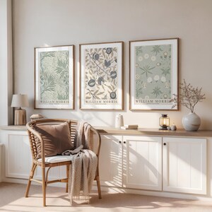 Può includere: Tre stampe artistiche incorniciate di William Morris con disegni botanici nei toni del verde, beige e blu. Le stampe sono esposte sopra un mobile bianco e una sedia in vimini con un cuscino marrone e una coperta beige.