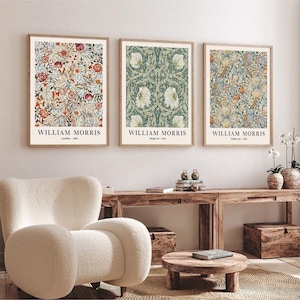 Peut inclure: Trois affiches encadrées de William Morris. Les impressions présentent des motifs floraux dans des tons de rouge, de bleu, de vert et de crème. Les cadres sont de couleur marron clair. Elles sont affichées au-dessus d'une console en bois et d'un fauteuil blanc.