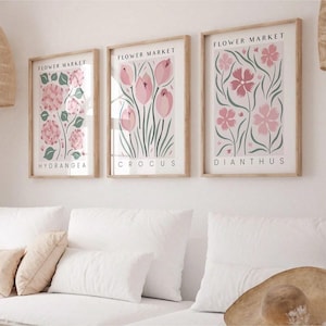 Könnte beinhalten: Drei gerahmte Kunstdrucke mit Blumen. Jeder Druck zeigt eine andere Blume: Hortensie, Krokus und Dianthus. Die Drucke haben einen hellen Holzrahmen und die Worte "Flower Market" oben. Die Blumen sind in Rosa- und Grüntönen auf weißem Hintergrund.