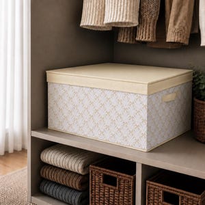 May include: A rectangular storage box with a cream-coloured lid and a patterned body featuring a repeating leaf design in cream and white. The box is on a shelf with folded blankets and woven baskets.