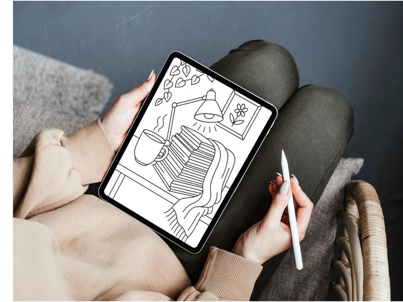 May include: A digital illustration on a tablet depicts a cozy scene with a stack of books, a steaming mug, and a desk lamp. A blanket drapes over the books. A stylus is held in the hand. The tablet is held on a person's lap.