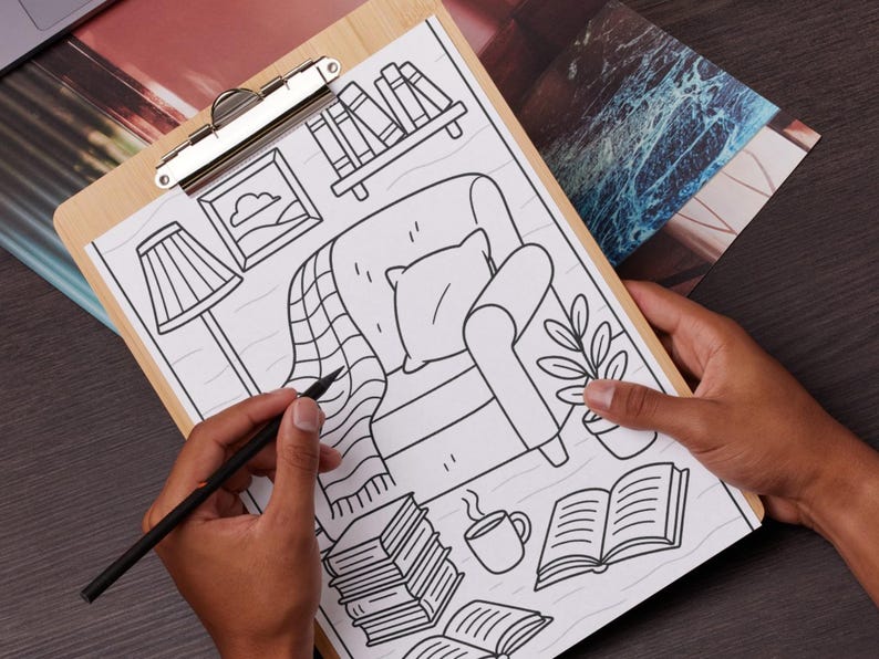 May include: A wooden clipboard holds a black and white illustration of a cozy living room scene. The drawing includes a chair, books, a lamp, and a plant. A hand holds a pencil, adding detail to the artwork.