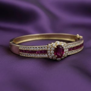 May include: Gold bracelet with an oval ruby centrepiece encircled by small diamonds. The bracelet has rows of rectangular rubies and small diamonds, set against a purple backdrop.