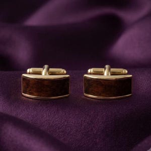 May include: A pair of rectangular cufflinks featuring a polished gold-tone metal frame and a dark brown wood grain inlay. The cufflinks have a curved front surface and a standard T-bar toggle mechanism on the back for secure fastening.