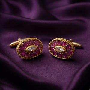 Puede incluir: Un par de gemelos ovalados de oro, cada uno con una piedra central transparente de talla marquesa rodeada por un grupo de pequeños rubíes redondos de color rosa rojizo intenso, engastados en un marco de oro texturizado con cierre.