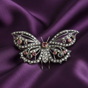 May include: A silver butterfly brooch with intricate detailing, set with diamonds, rubies, and sapphires. The brooch has a central ruby and gold accents. The wings are open, and the brooch is displayed on a purple satin fabric.
