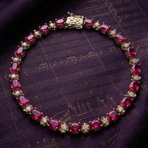 May include: A gold bracelet featuring oval-cut red gemstones and small white gemstones. The bracelet is set on a dark purple background with musical notes.