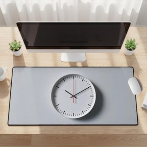 May include: A modern desk setup featuring a large computer monitor, a gray desk mat with a white clock, and a white mouse. The clock has black hands and a red second hand. Small potted plants are on the desk.