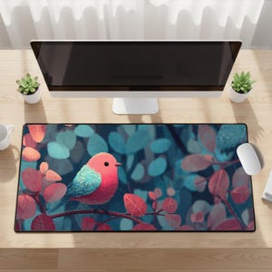 以下が含まれることがあります： 赤い葉の枝に止まっている鳥のカラフルなイラストが描かれた長方形のマウスパッド。背景には青とターコイズの葉があります。マウスパッドは、コンピューターとアクセサリーを備えた木製の机の上にあります。