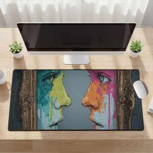 May include: A rectangular mouse mat with a colourful artistic design of two faces in profile, each with vibrant paint-like streaks. The faces are framed by ornate gold-coloured borders, set against a grey background.