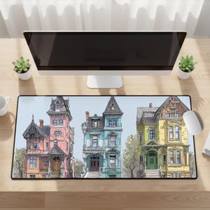 May include: A rectangular mouse pad featuring a watercolor illustration of three Victorian houses in pink, blue, and yellow. The houses have detailed architectural features and are set against a light blue background.