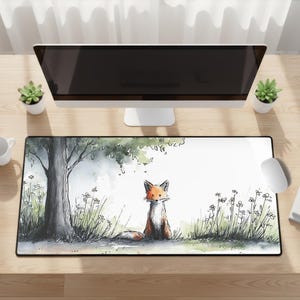 May include: A rectangular desk mat featuring a watercolor illustration of a fox sitting under a tree. The fox has orange and white fur, with a black outline. The background includes grass, flowers, and a light green tree canopy.