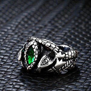 May include: A silver ring with a snake design. The ring has a large, oval-shaped, bright green gemstone at its centre. The snake's head and body wrap around the finger, creating a unique and detailed accessory.