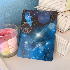 May include: A rectangular card featuring a deep blue space scene with a floating astronaut, planets, and stars. The text reads "WHO IS GRACE TALKING TO QUESTION", "GRACE ROCKS LOVE STARS", "TO SEE HUMAN TECHNOLOGY", and "AMAZE AMAZE AMAZE" in white.