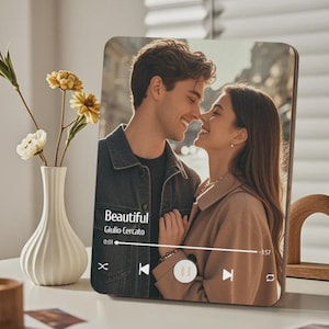 Puede incluir: Impresión fotográfica en madera que muestra a una pareja sonriendo. La impresión muestra una interfaz de reproductor de música con el título de la canción "Beautiful" de Giulio Cercato. Un jarrón blanco con flores amarillas está en el fondo.