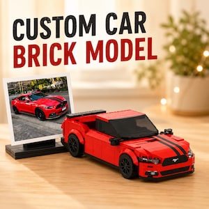 Op de afbeelding: Een rood modelauto van bouwstenen met zwarte racestrepen, zwarte wielen en een zwarte spoiler. Naast de auto staat een kleine ingelijste foto van een echte rode sportwagen. De tekst CUSTOM CAR BRICK MODEL staat in grote letters weergegeven.