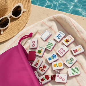 May include: A set of white mahjong tiles with colourful illustrations and text, including Joker, North, and various numbers, spilling from a bright pink drawstring bag. The tiles feature floral, dragon, and bamboo designs alongside a small die.