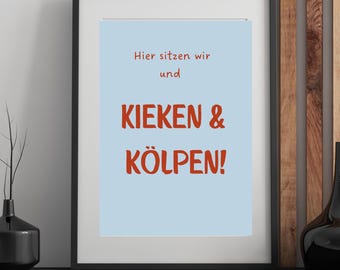 May include: Framed art print with a light blue background and red text that reads "Hier sitzen wir und KIEKEN & KÖLPEN!". The black frame sits on a black surface, with a wooden background.