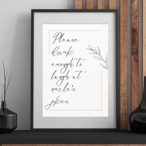 Könnte beinhalten: Gerahmter Druck mit dem Text "Please drink enough to laugh at uncle's jokes" in einer stilvollen Schriftart. Der Druck befindet sich in einem schwarzen Rahmen und weist ein dekoratives Blumenelement auf. Der Hintergrund ist strukturiertes Off-White.