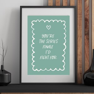 Könnte beinhalten: Gerahmter Kunstdruck in einem schwarzen Rahmen. Der Druck hat einen tealfarbenen Hintergrund mit weißem Text: "You're the series finale I'd fight for." Ein weißes Herz befindet sich über dem Text. Der Druck liegt auf einem schwarzen Regal.