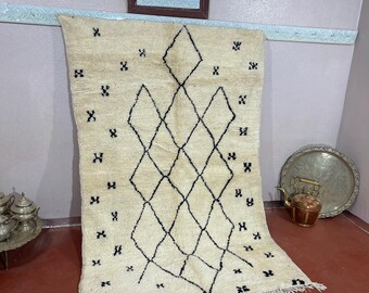 May include: Cream-colored rug with a black diamond pattern and small black accents. The rug has a fringe along the bottom edge. The rug is hanging on a wall with a mirror and decorative trim.