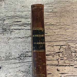 May include: A vintage brown leather-bound book with gold lettering on the spine that reads "KIRKHAM'S GRAMMAR 1827".