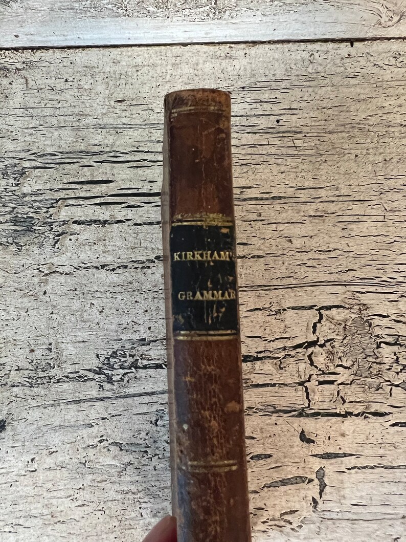 May include: A vintage brown leather-bound book with gold lettering on the spine that reads "KIRKHAM'S GRAMMAR 1827".