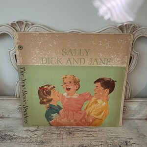 May include: A vintage hardcover book titled Sally, Dick and Jane, The New Basic Readers. The cover features a tan and green background with an illustration of three children laughing. The book shows signs of wear with scuffing on the surface.
