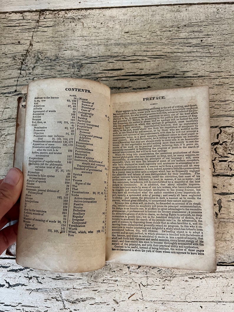 May include: An open book with a yellowed, aged appearance. The pages contain a table of contents with headings such as "Nouns", "Gender of", "Person of", "Number of", "Case of", "Orthography", "Parsing", "Participles", "Prepositions", "Pronouns", "Personal", "Compound Personal", "Relative", "Pronounciation", "Prosody", "Provincialisms", "Punctuation", "Rhetorick", "Rules of Syntax", "Sentences", "Terminations", "Transposition", "Standard of Grammatical Syntax", "To", "Tenses", "Signs of the", "The", "That", "Verbs", "Active-Transitive", "Active-Intransitive", "Passive", "Neuter", "Defective", "Auxiliary", "Irregular", "Compound", "Regular", "Versification", "Worth", "What, which, who", "You".