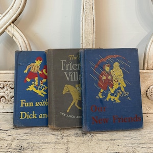 May include: Three vintage children's books with colorful illustrations. The books have blue and gray covers with titles including "Fun with Dick and", "The Friend Villa", and "Our New Friends". The books are arranged on a distressed white surface.
