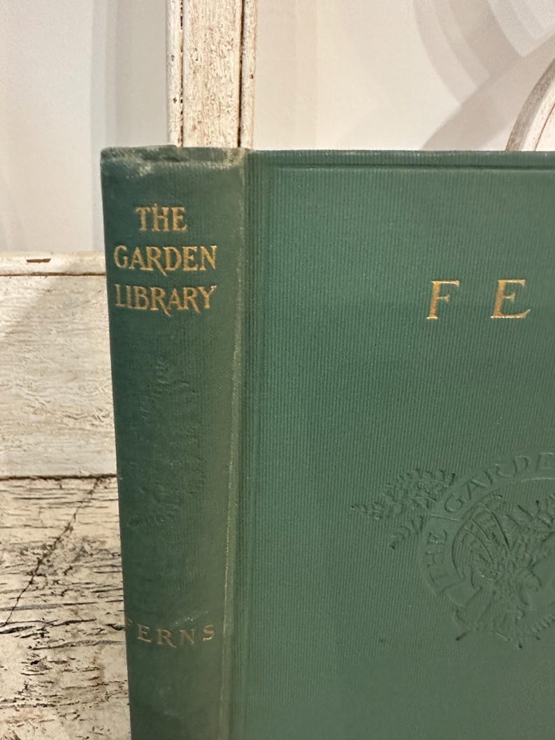 May include: A vintage green book from "The Garden Library" series, featuring gold lettering and embossed botanical illustrations. The book's spine reads "Ferns."