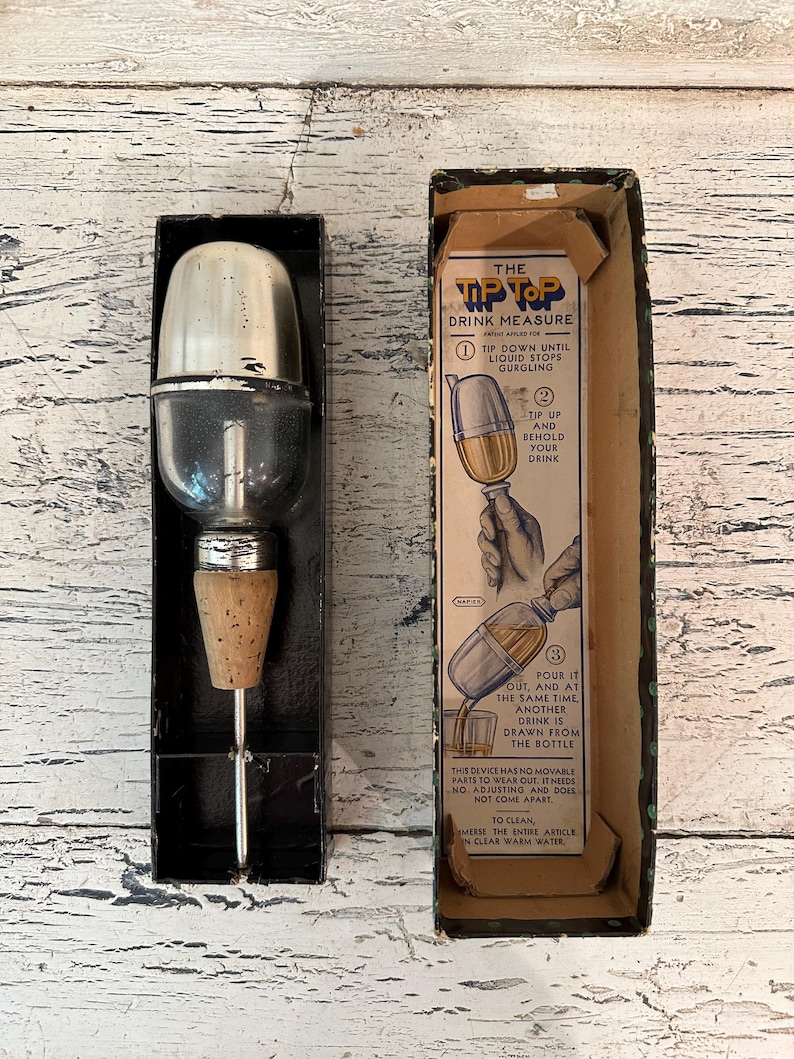 May include: Vintage Tip Top Drink Measure in its original box. The device is made of glass and metal and has a cork stopper. The box is brown with blue and white text and illustrations showing how to use the device.