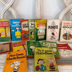 May include: A collection of fourteen vintage Peanuts paperback books by Charles M. Schulz, featuring colorful illustrated covers with characters like Charlie Brown and Snoopy. Titles include You're a Winner, Charlie Brown, Good Ol' Snoopy, and others.