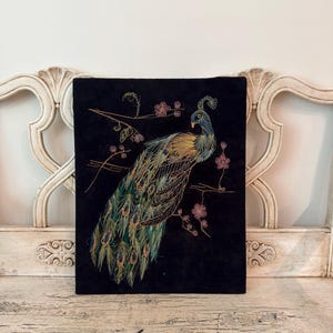May include: A rectangular black wall art piece featuring a detailed string art design of a peacock. The peacock is rendered in shades of blue, green, and gold thread, perched on a branch with small pink flowers against a dark background.